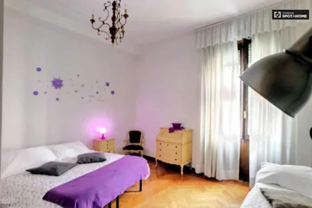 A bedroom with two beds, a chandelier, a dresser, and a window with curtains.