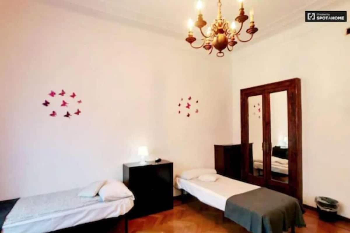 A bedroom with two single beds, a wooden floor, a chandelier, a mirror, and wall decorations.