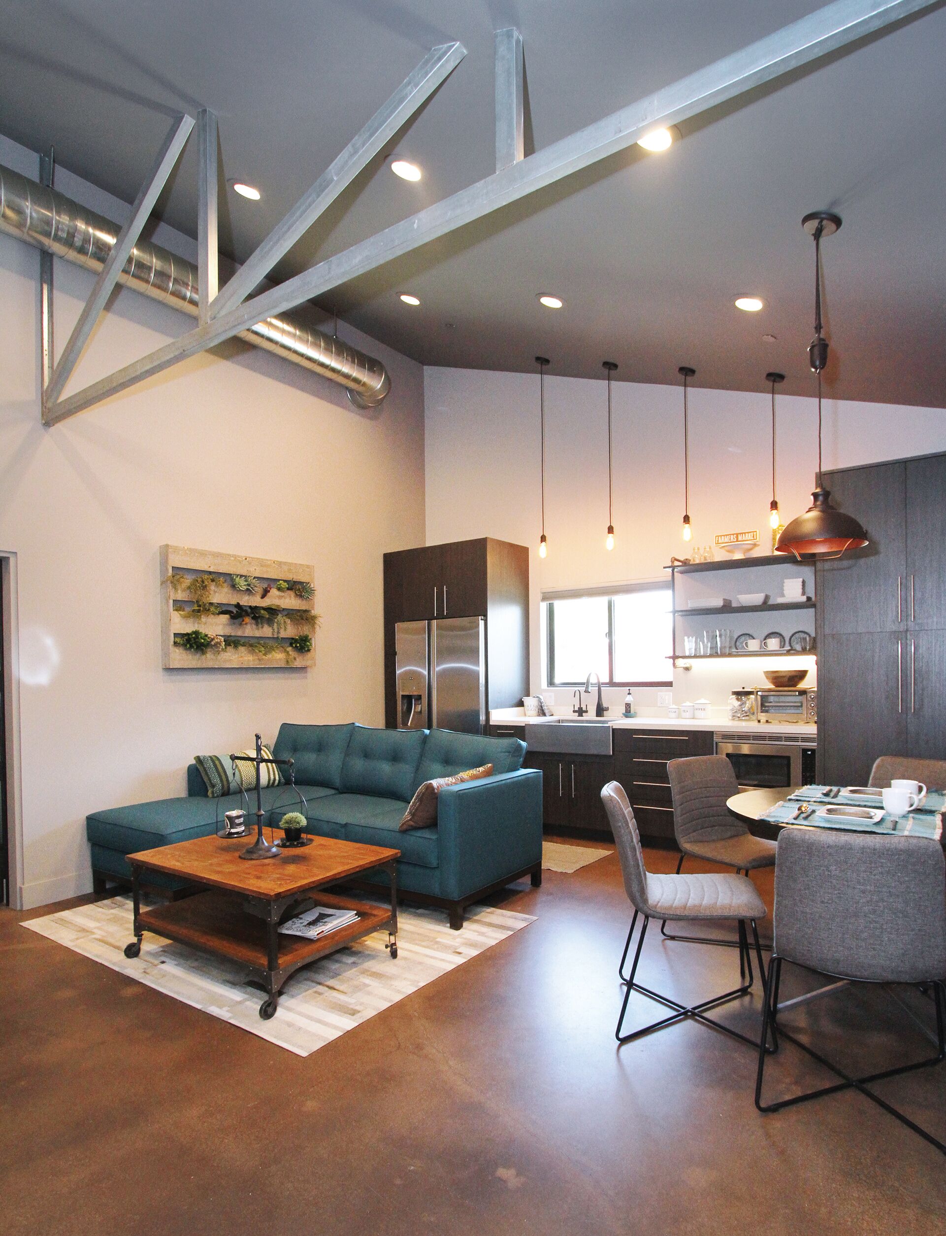 A modern living room with a sofa, coffee table, and dining area with chairs. There is a kitchen in the background with a sink and appliances.