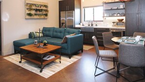 Uma sala de estar moderna com sofá, mesa de centro e área de jantar com cadeiras. Uma cozinha ao fundo, com pia e eletrodomésticos.