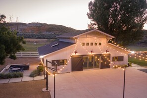 A barn-like building with a covered outdoor area, a fenced yard, and a large tree.