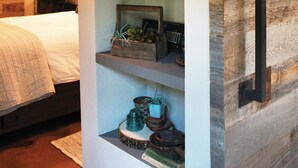 Quarto com cama, mesa de cabeceira e prateleira na parede com objetos decorativos.