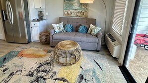 Una sala de estar moderna con un sofá gris, almohadones decorativos, una mesa de centro tejida y un cuadro en la pared.