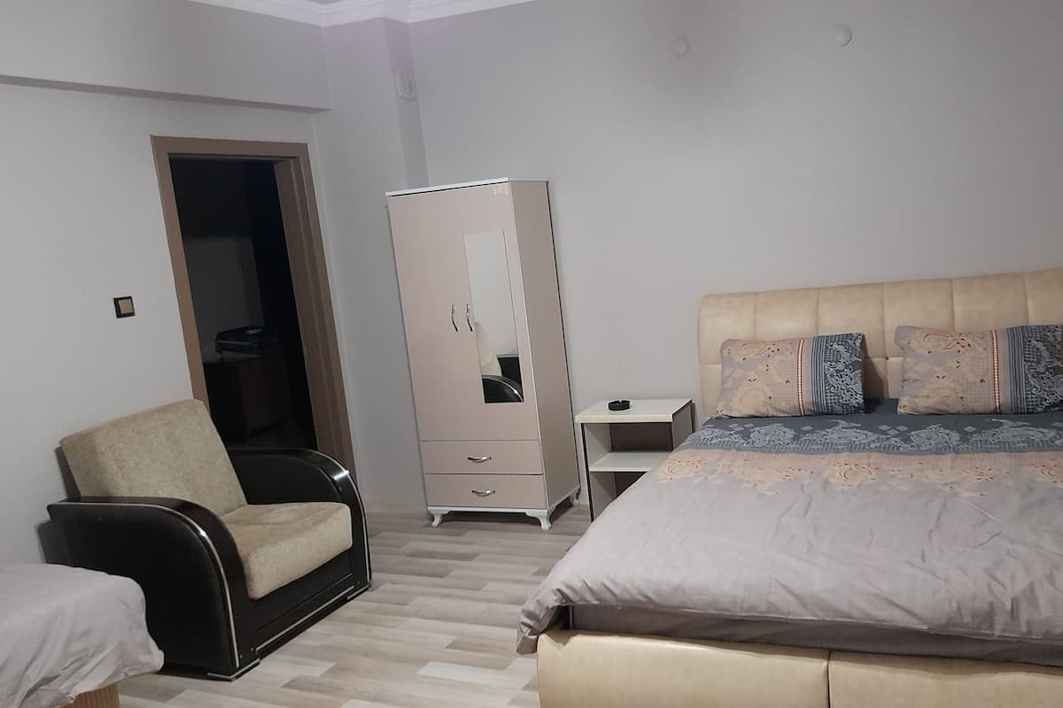 A bedroom with a bed, a chair, a wardrobe, and a desk.