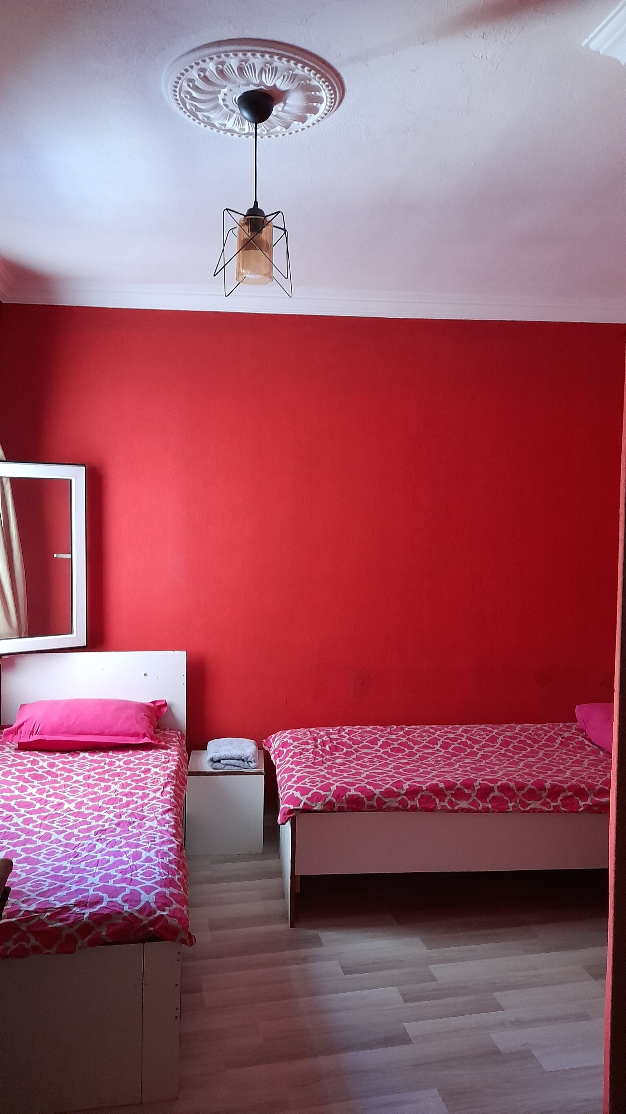 A bedroom with two beds, a red wall, a ceiling fan, and a mirror.