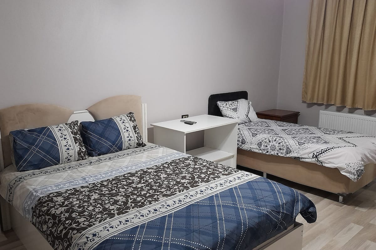 A bedroom with two beds, a bedside table, and a radiator.