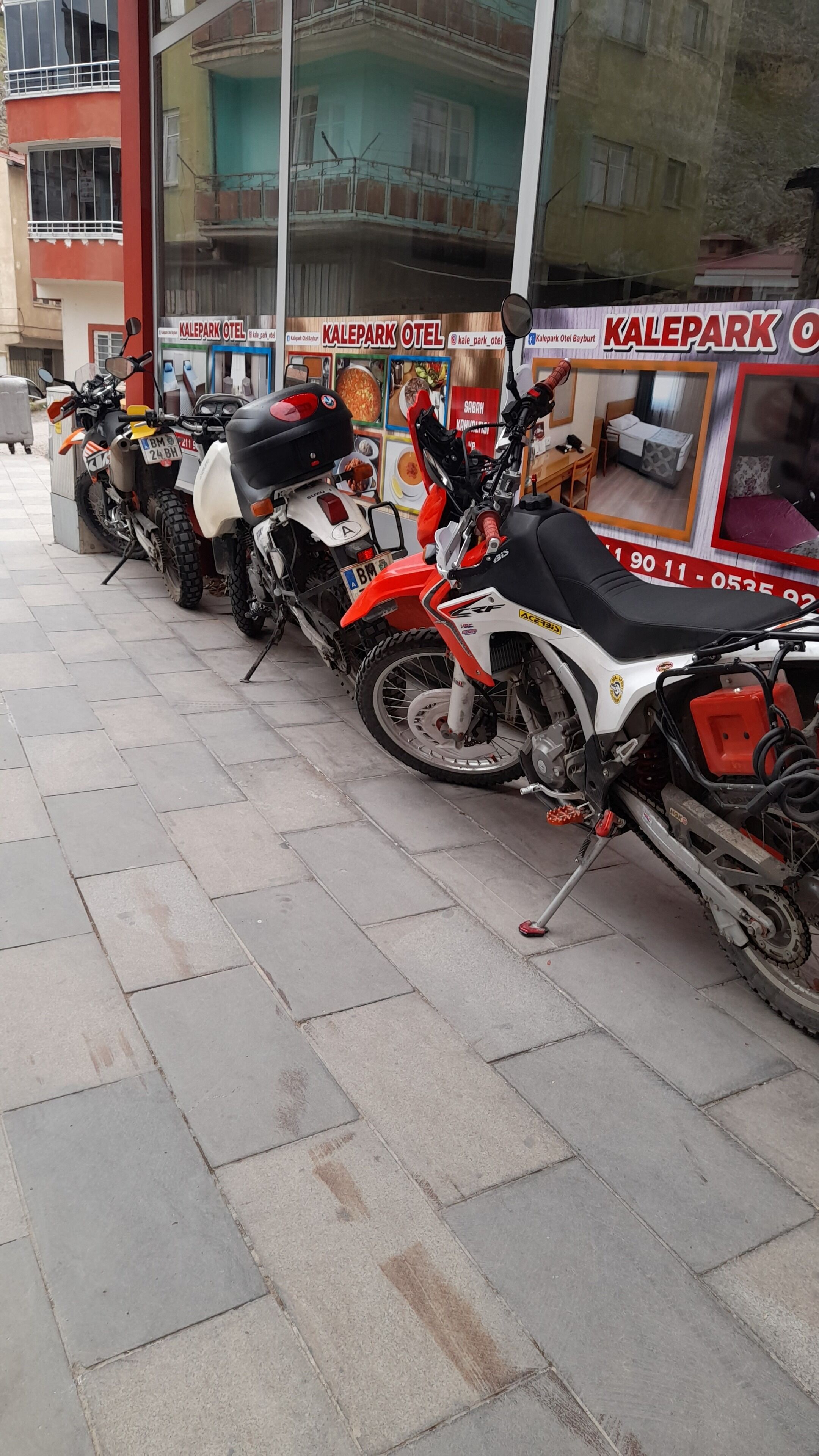 A row of parked motorcycles in front of a building with a sign that reads "KalePark Hotel".