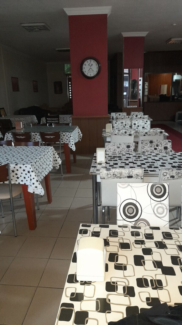 Un comedor con mesas cubiertas de manteles estampados, un reloj en la pared y sillas dispuestas alrededor de las mesas.