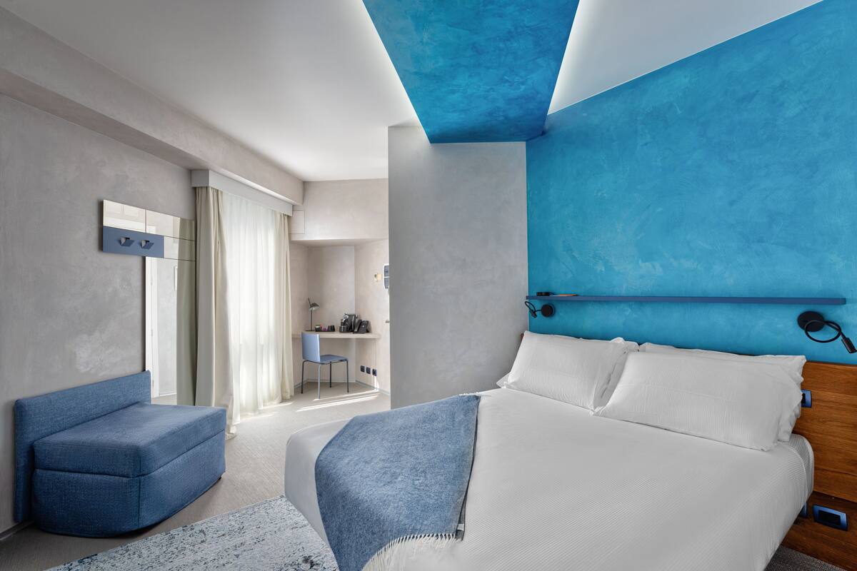 A modern bedroom with a bed, a blue armchair, and a desk with a chair.