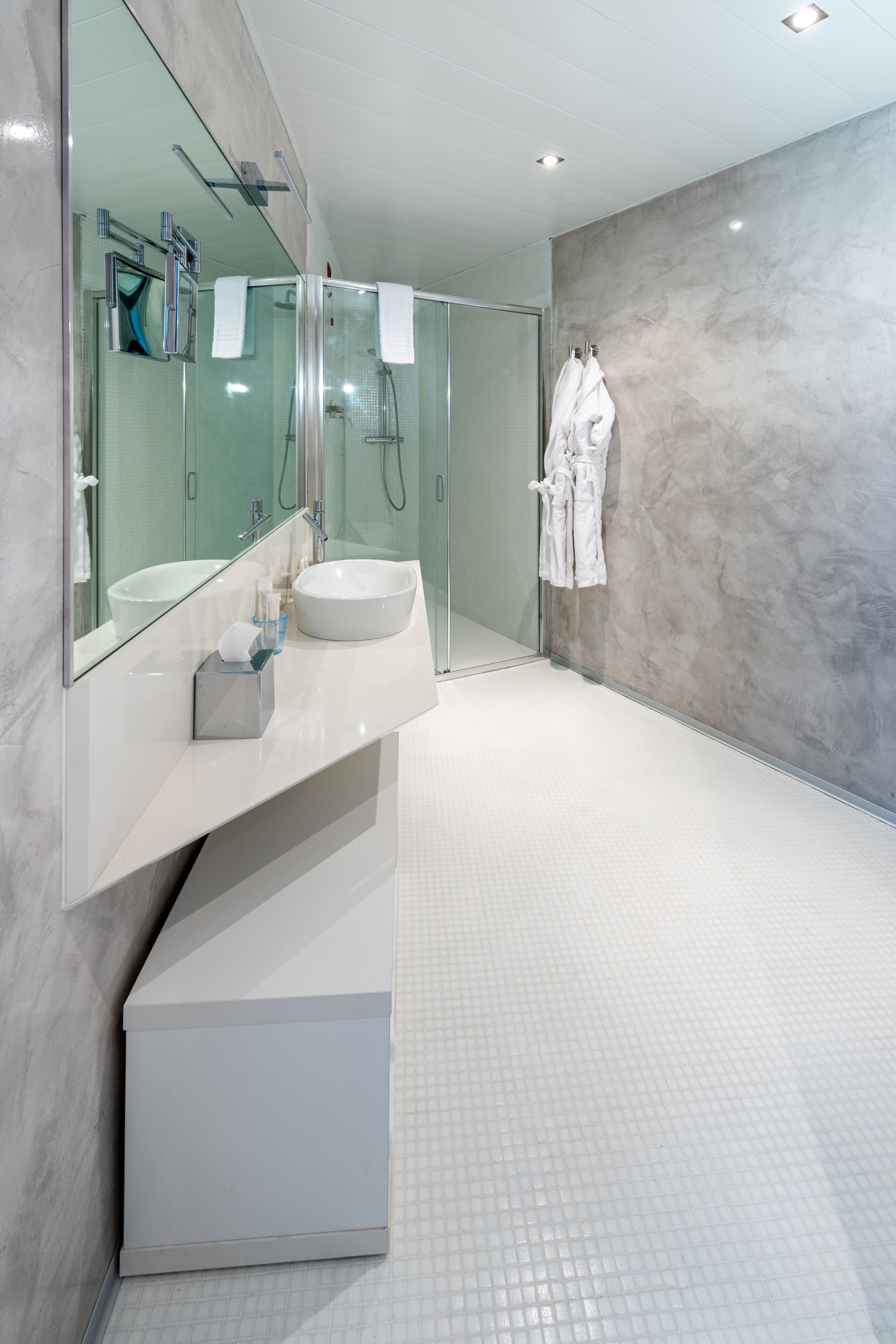 Une salle de bain moderne avec un grand miroir, un lavabo blanc et une douche à parois de verre.