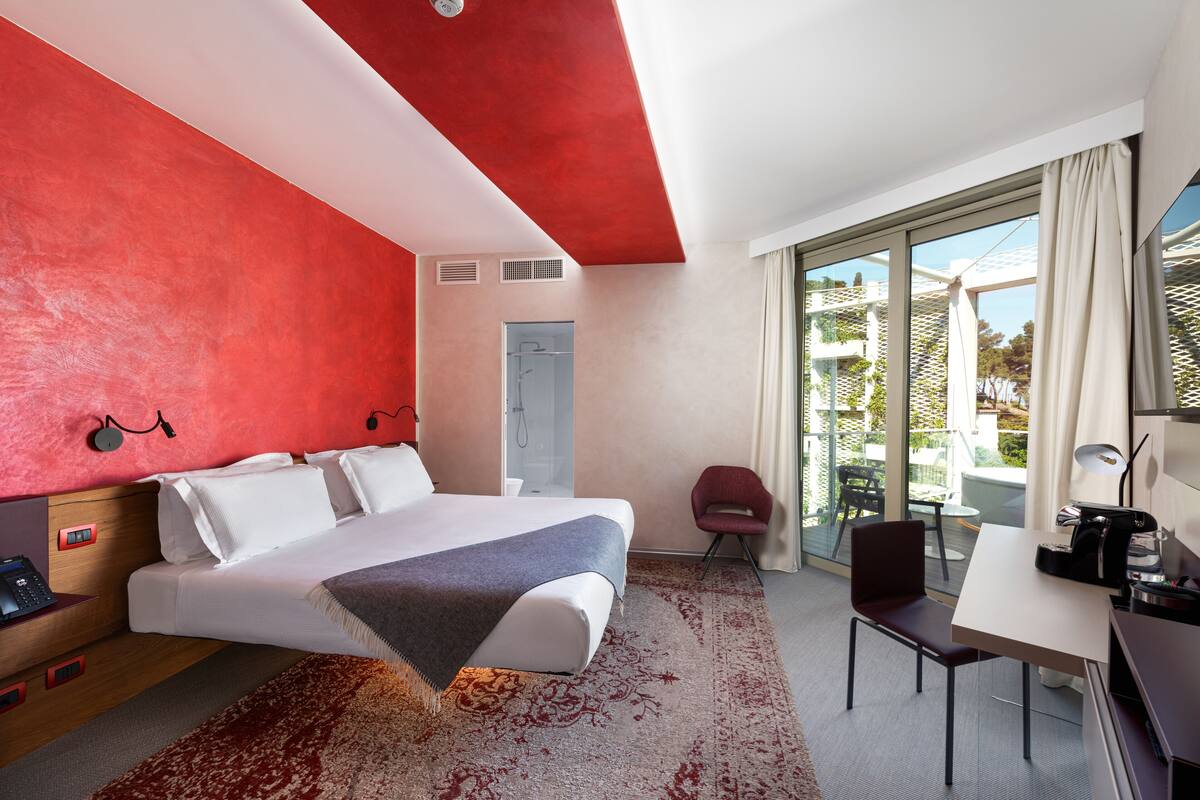 A hotel room with a large bed, a desk, a chair, and a view of the outdoors.