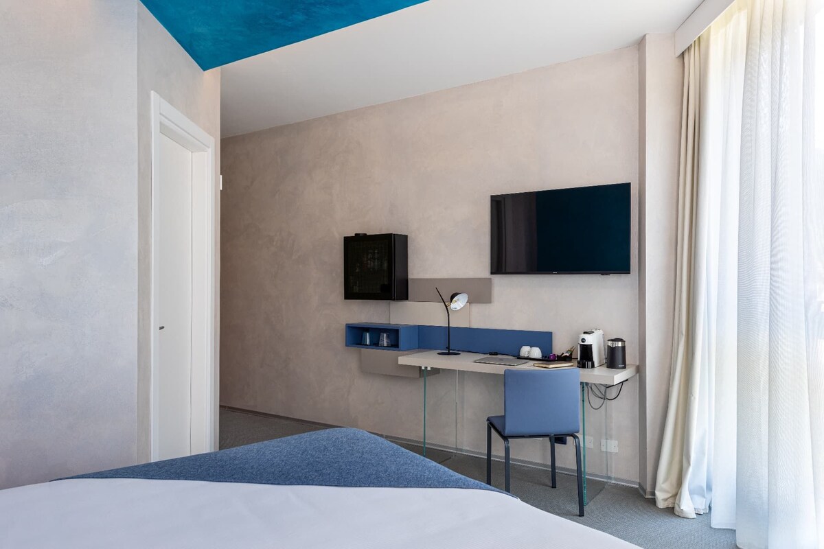 Una habitación de hotel con una cama, un escritorio con silla, un televisor y una cafetera.