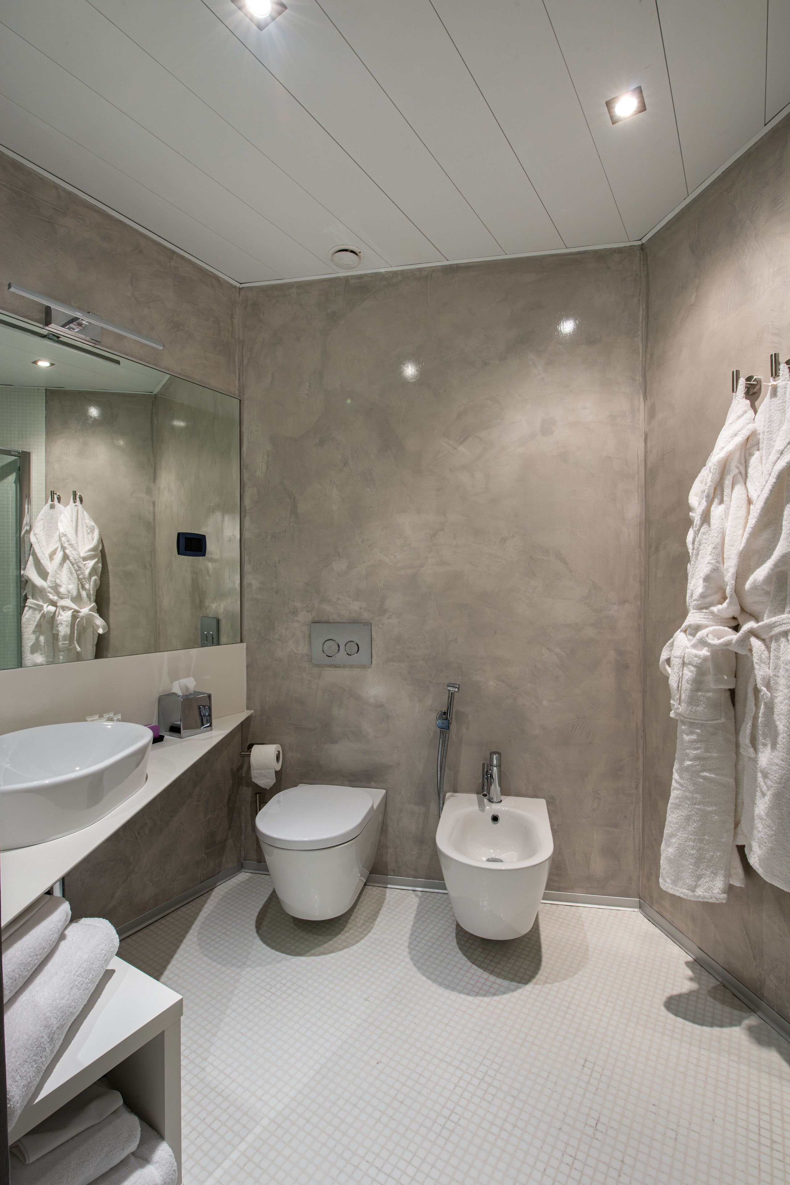 Ein modernes Badezimmer mit einem großen Spiegel, einem Bidet, einer Toilette und einem Waschbecken.