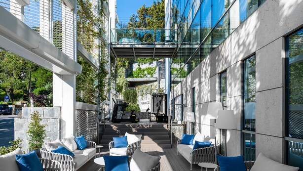 An outdoor seating area with white sofas and blue cushions, a wooden deck, and a glass building facade. - Carrick Hotel Camogli Portofino Coast (Camogli)