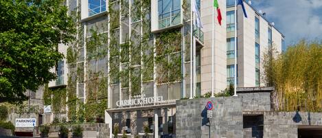 A modern hotel with a stone facade, multiple flags, and a parking sign.