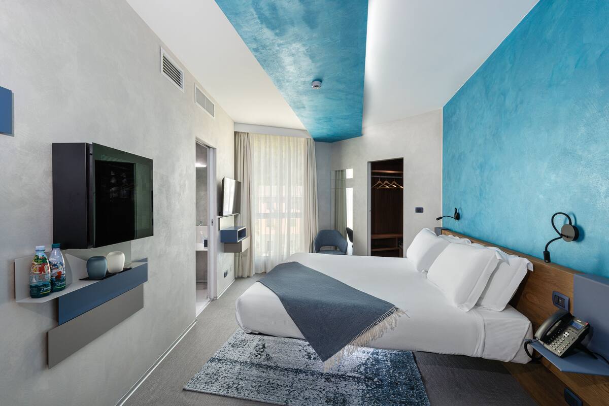A modern hotel room with a large bed, a flat-screen TV, a bedside phone, and a wardrobe.