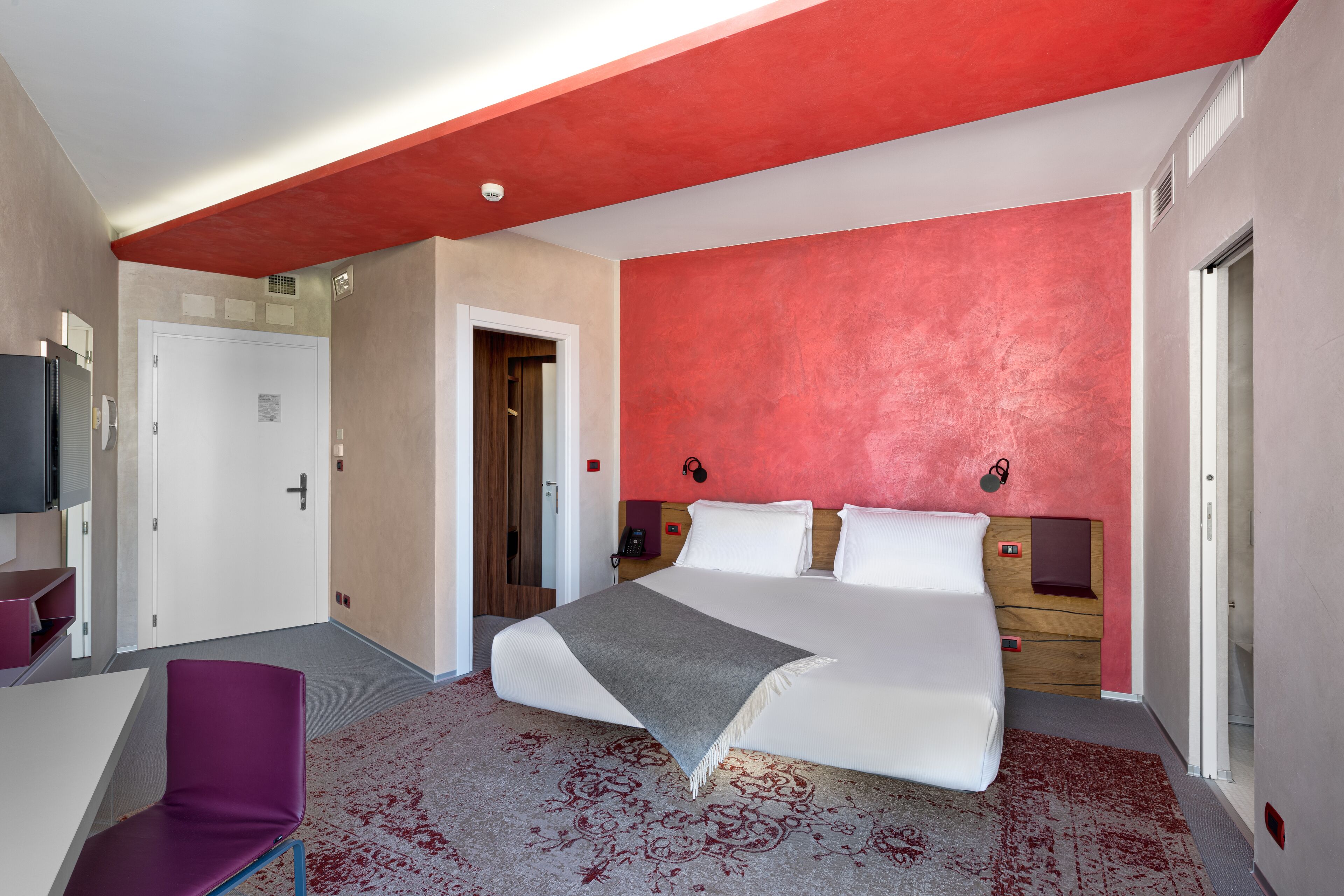 A modern hotel room with a large bed, a desk, and a chair.