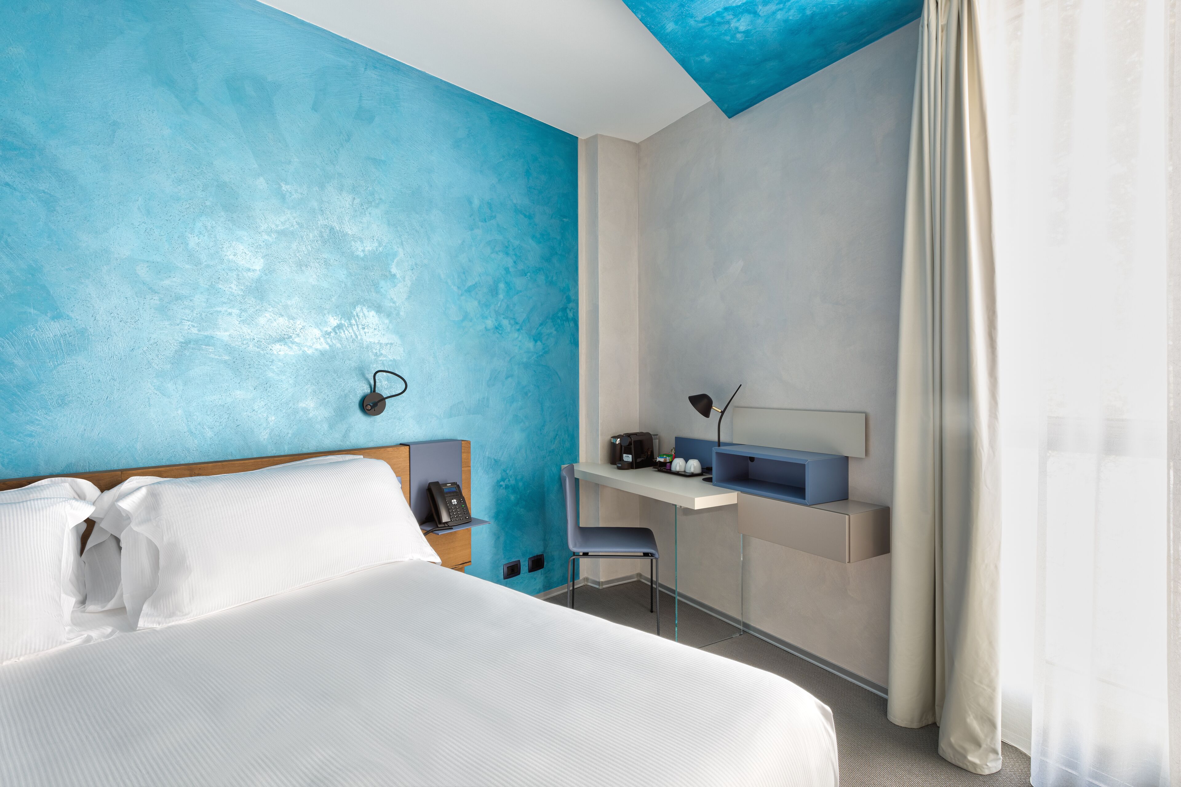 A hotel room with a bed, a desk, and a chair.