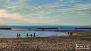 Ein Strand mit Menschen, die laufen und stehen, einem klaren Himmel und fernen Bergen.