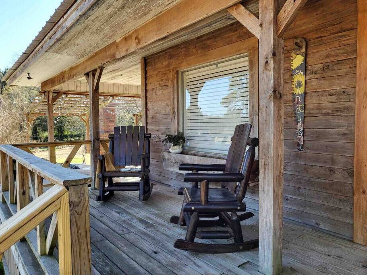 A wooden porch with two rocking chairs and a table, overlooking a garden.