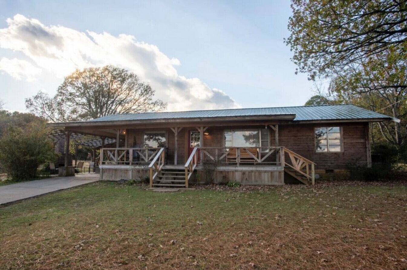 Een rustieke blokhut met een veranda, houten trap en een metalen dak.
