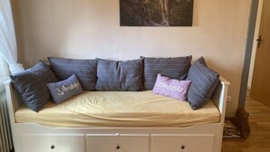 Un canapé blanc avec un coussin beige, plusieurs coussins gris et un petit coussin violet orné d’un motif.