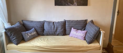 Ein weißes Sofa mit einem beigen Kissen, mehreren grauen Kissen und einem kleinen violetten Kissen mit Text.