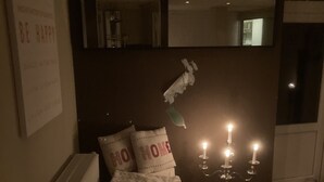 Une pièce faiblement éclairée, avec un lit, un radiateur, un miroir fixé au mur et un chandelier avec des bougies.