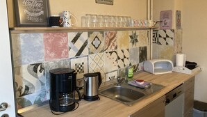 Une cuisine équipée d’une machine à café, d’une bouilloire et d’un évier. On y trouve des tasses et des verres sur le comptoir, ainsi qu’un panneau indiquant : « Le meilleur café du matin. »