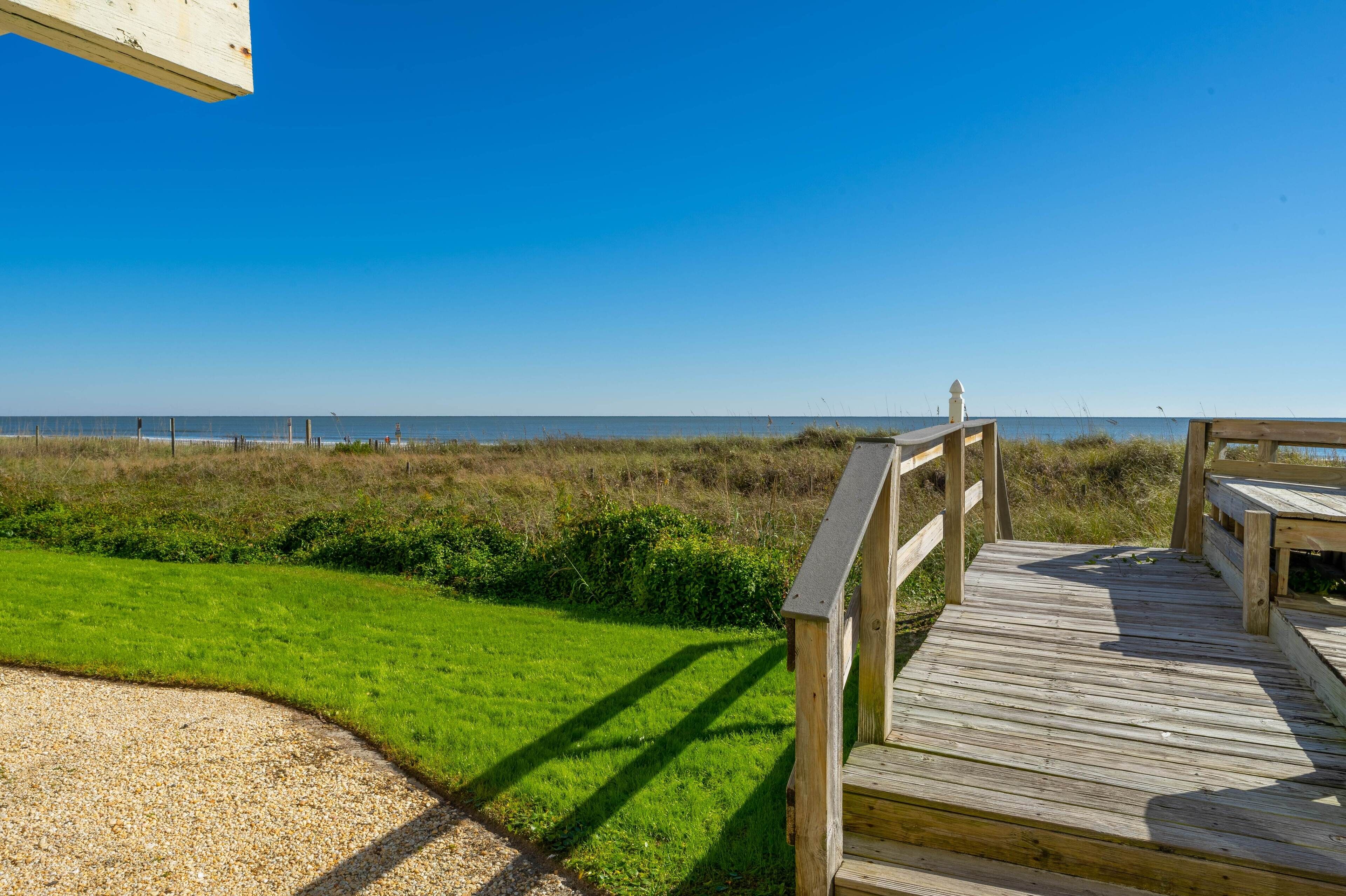 A wooden deck leading to a beach with a clear view of the ocean.