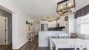 Eine moderne Küche mit weißen Schränken, einer zentralen Kochinsel und einem Essbereich mit weißen Stühlen.