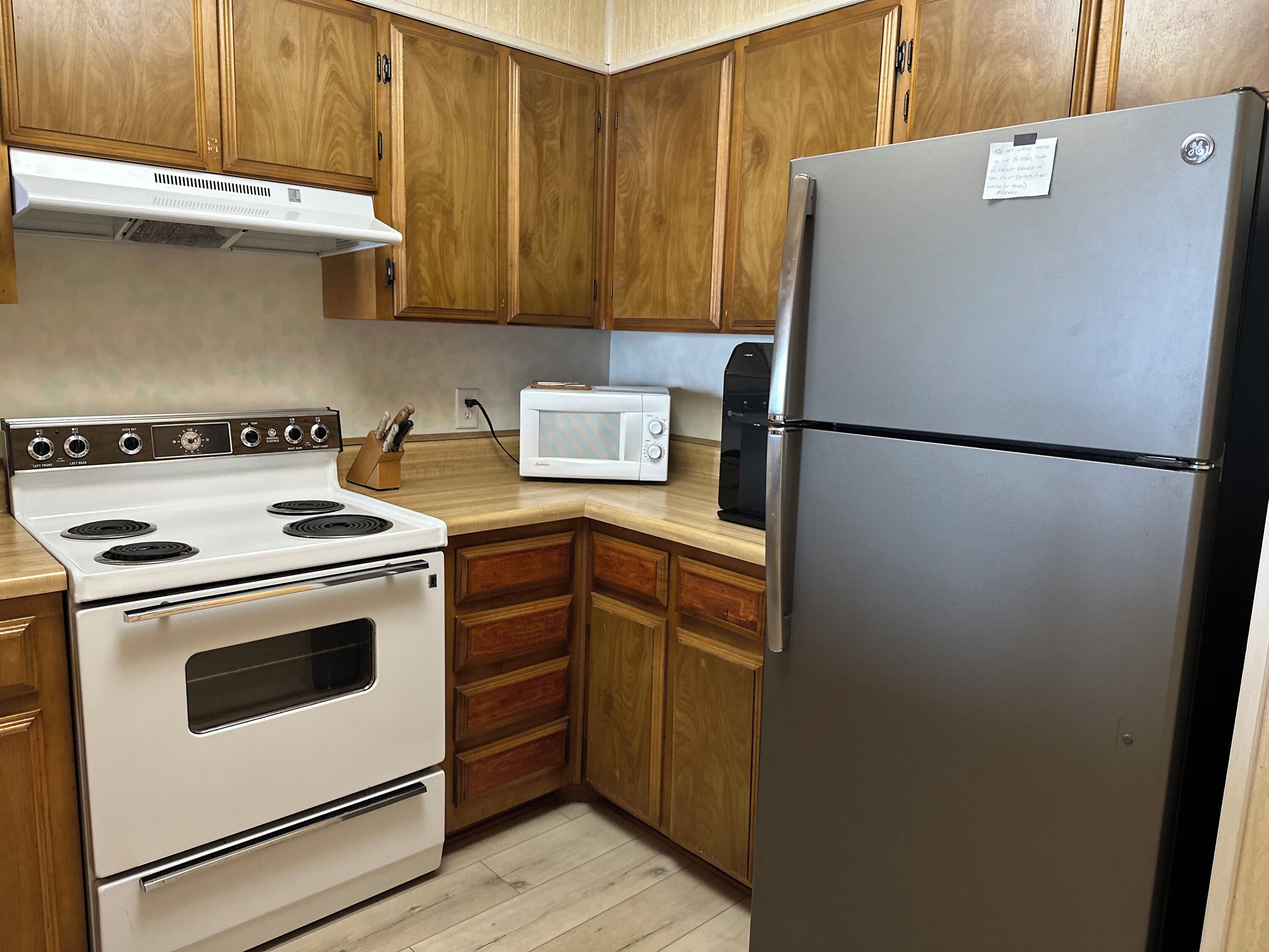 A kitchen with wooden cabinets, a stainless steel refrigerator, a white stove, and a microwave.