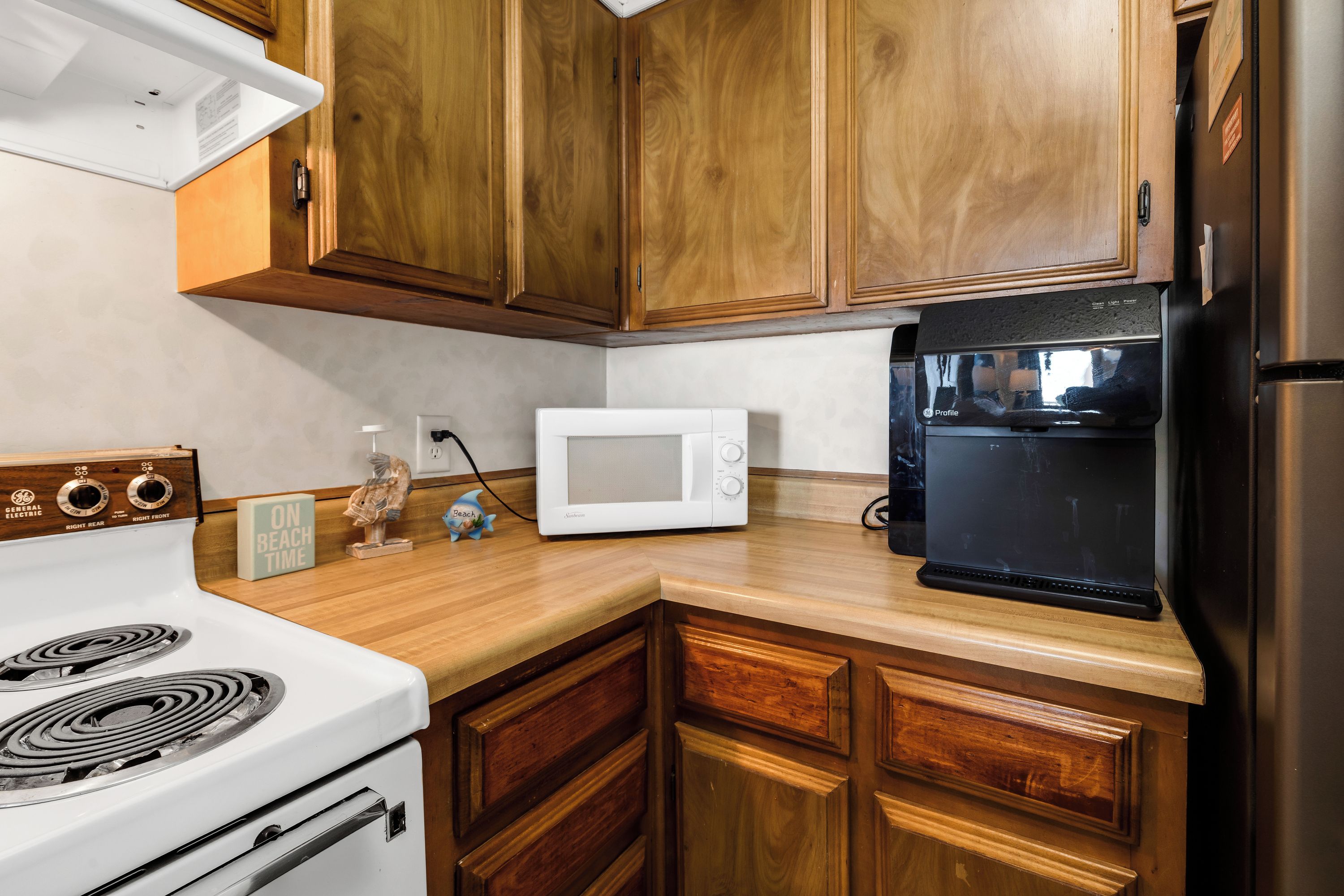 Una cucina con mobili in legno, un piano cottura bianco, un forno a microonde e un frigorifero nero.