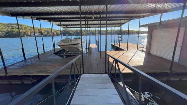 A covered dock with a boat, a metal railing, and a view of the lake. - PEACEFUL HOME-4 BEDROOMS, 3 KING BEDS, 4 BATHROOMS, EASY PARKING & A BOAT SLIP! (Camdenton)