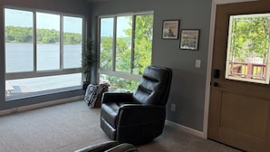 A room with large windows, a black leather chair, a potted plant, and a door with a view of a lake. - PEACEFUL HOME-4 BEDROOMS, 3 KING BEDS, 4 BATHROOMS, EASY PARKING & A BOAT SLIP! (Camdenton)
