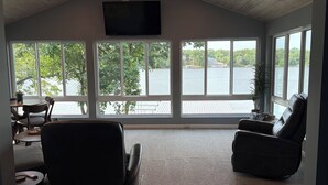 A room with a large window overlooking a body of water, a ceiling fan, and a flat-screen TV mounted on the wall. - PEACEFUL HOME-4 BEDROOMS, 3 KING BEDS, 4 BATHROOMS, EASY PARKING & A BOAT SLIP! (Camdenton)