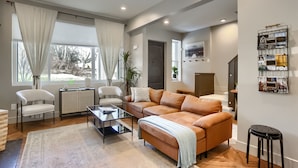 Ein modernes Wohnzimmer mit einer Ledersofa, einem Glastisch und einem Essbereich mit weißem Tisch und Stühlen.