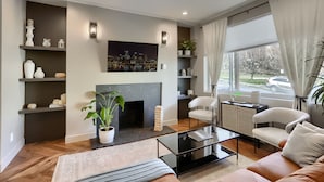 Ein modernes Wohnzimmer mit Kamin, Regalen mit Dekorationsobjekten, einem Couchtisch und Blick ins Freie.