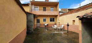 A narrow courtyard with a table and chairs, a small window, and a door.