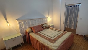 A bedroom with a bed, nightstands, a chair, a door with curtains, and a wall-mounted light fixture. - RURAL ENVIRONMENT, land of fields and vineyards.GORDONCILLO (Gordoncillo)