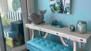 Ein Zimmer mit einer hellblauen Bank, einem weißen Konsolentisch mit Dekoration und einem großen abstrakten Gemälde an der Wand.