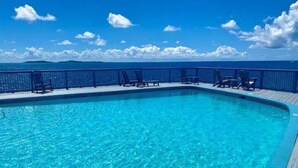 Ein klares, blaues Schwimmbecken mit Liegestühlen und einer Holzterrasse, umgeben von einem Zaun.