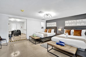 Habitación de hotel con dos camas, zona de estar, comedor y baño.
