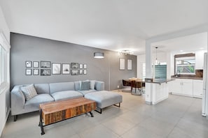 Una sala de estar moderna con un sofá gris, una mesa de centro de madera y un comedor con mesa y sillas.