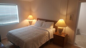 A neatly made bed with white bedding, two bedside lamps, and a wooden nightstand. - Port Charlotte House on the Canal   (Port Charlotte)