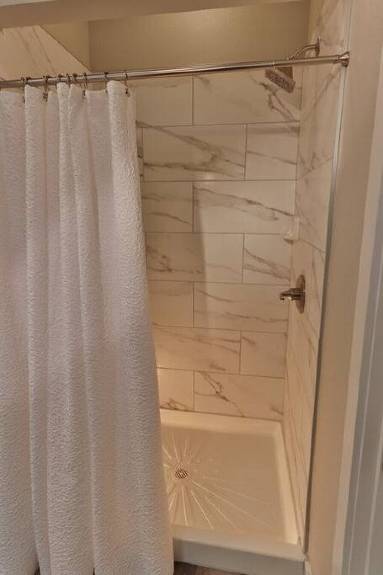 Un espace douche doté d ’une porte en verre, de carreaux de marbre et d’un rideau de douche blanc.