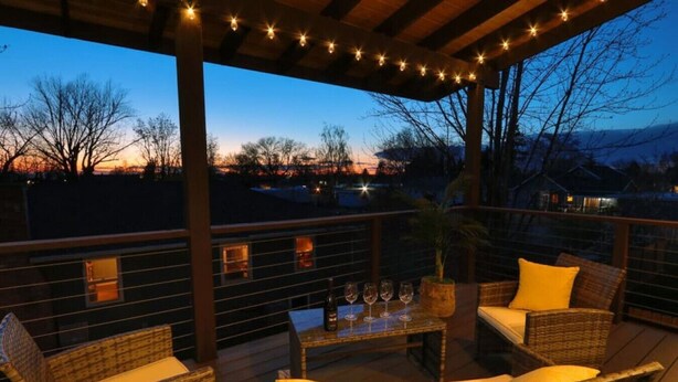 Un espace extérieur aménagé en terrasse, avec des meubles en osier et des guirlandes lumineuses, offrant une vue sur un paysage pittoresque.