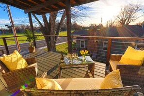 A covered outdoor seating area with wicker furniture, a glass table with a vase of yellow flowers, and a bottle. - Fieldview | A Spacious Stay Near WWU & Downtown (College Place)