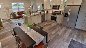 Une cuisine moderne avec un coin repas, comprenant un îlot central, des appareils en acier inoxydable et une vue sur un jardin.