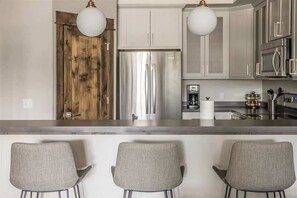 Una cocina moderna con electrodomésticos de acero inoxidable, armarios blancos y una isla central con taburetes de bar.